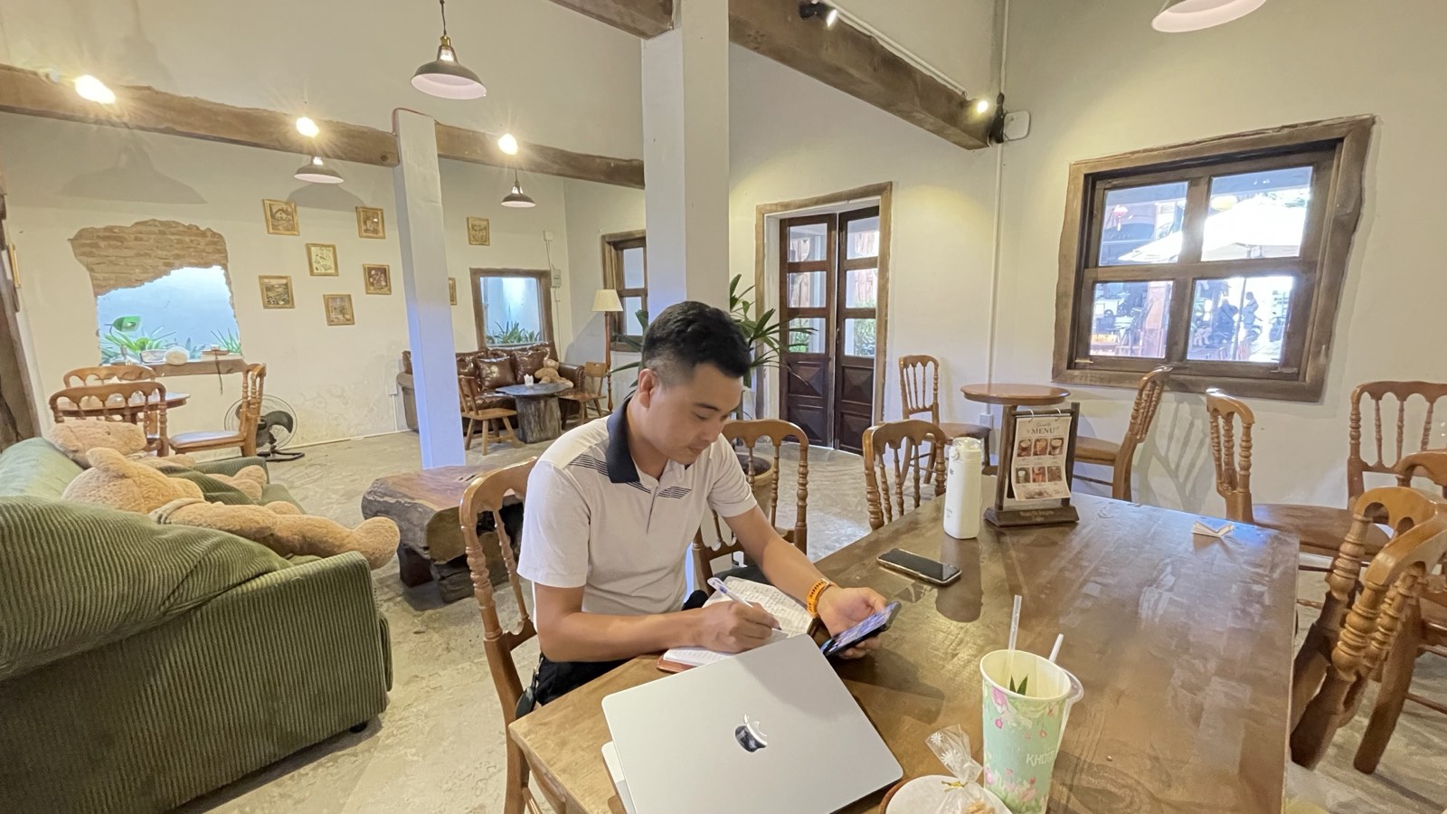 Khuất Anh Dũng ngồi ghi sổ tay tại một quán cà phê mộc ở Nha Trang